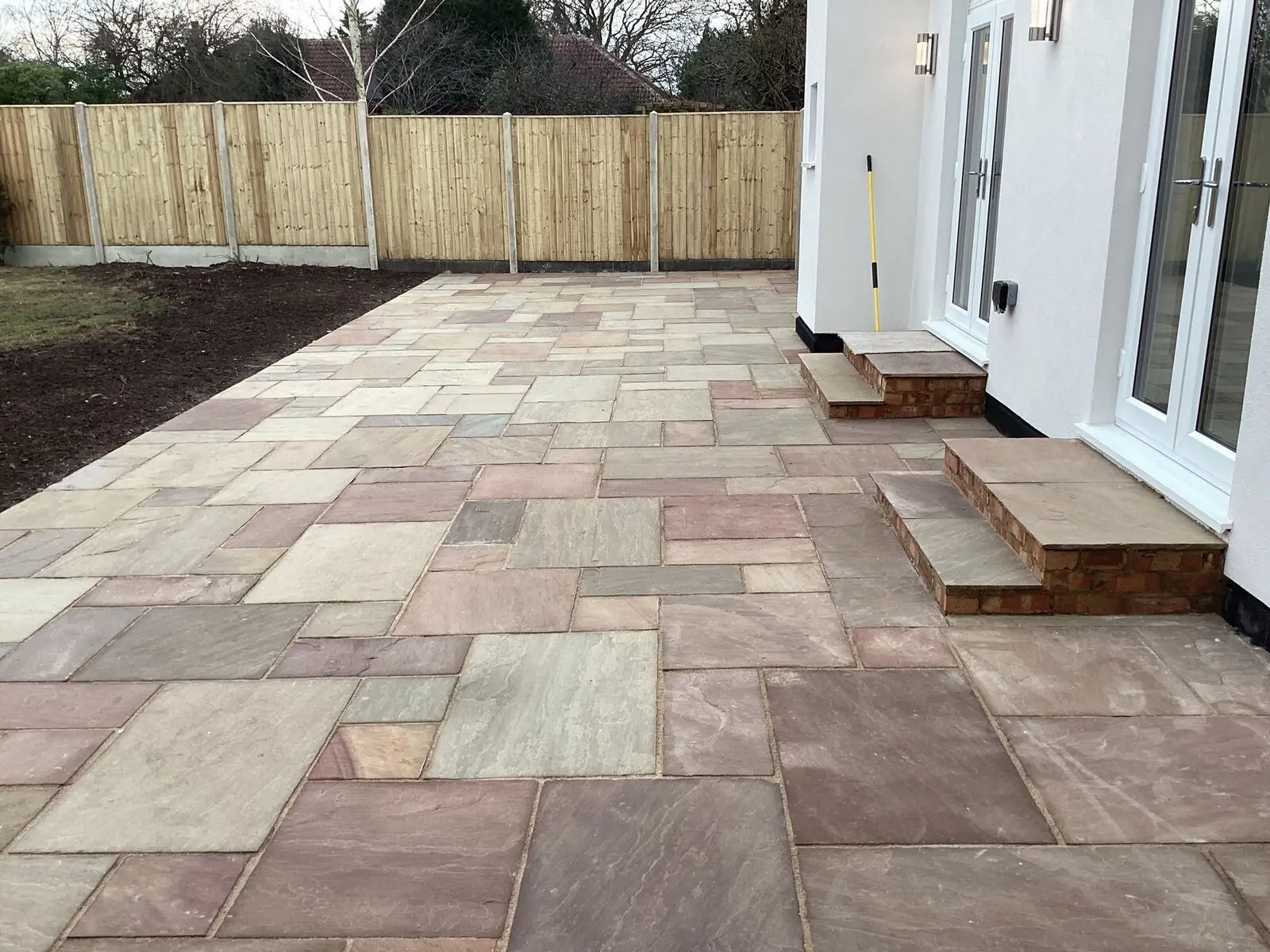 Sandstone patio with built-in steps running along the side of a white rendered house